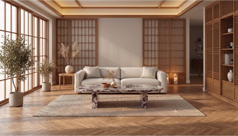 Op de afbeelding: Een woonkamer met een cr&egrave;mekleurige bank, een lage marmeren salontafel met donkere aders en een getextureerd vloerkleed. De ruimte bevat houten latwerk-scheidingswanden, een houten boekenplank en twee olijfbomen in potten op een visgraatvloer.