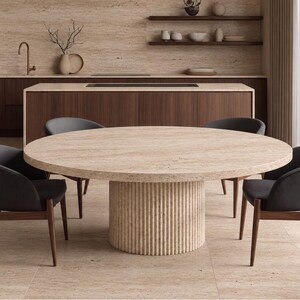 May include: A round dining table with a beige travertine top and a cylindrical, fluted base, surrounded by four dark grey upholstered chairs with wooden legs. The table features a natural stone texture with visible porous patterns.