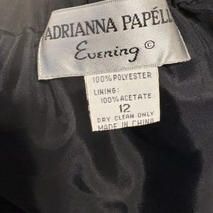 Puede incluir: Primer plano de una prenda negra con etiqueta. La etiqueta dice "ADRIANNA PAPELL Evening" y enumera los materiales como 100% poli&eacute;ster y forro 100% acetato. Tambi&eacute;n indica la talla 12 y "DRY CLEAN ONLY" con "MADE IN CHINA".