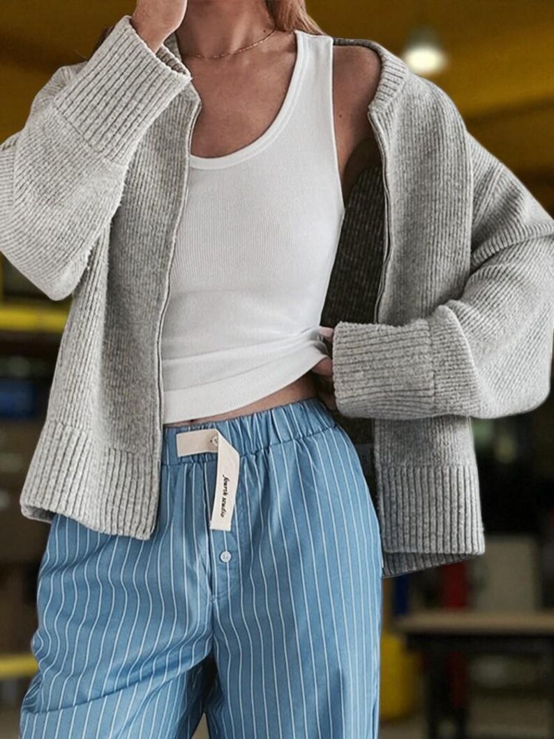 Peut inclure: Un cardigan gris clair, un d&eacute;bardeur blanc et un pantalon de pyjama bleu &agrave; rayures. Le pantalon a une fermeture boutonn&eacute;e et une &eacute;tiquette "Journa Studio". Le cardigan a des poignets c&ocirc;tel&eacute;s et une fermeture &eacute;clair.