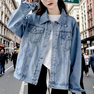 May include: Pale blue denim jacket featuring a button-down front, two chest pockets, and a classic collar. The jacket has long sleeves and a relaxed fit. The denim is a medium wash. The jacket is new.