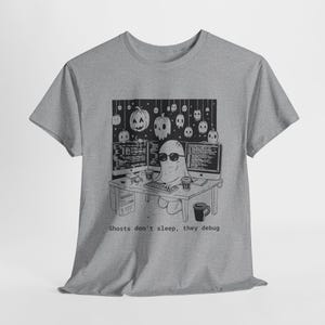 May include: A grey t-shirt with a black and white graphic of a ghost wearing sunglasses, coding at a desk with two computer monitors. The text "Ghosts don't sleep, they debug" is below the graphic. Halloween themed.