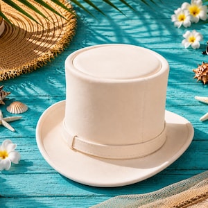 May include: A cream-colored top hat with a band, resting on a turquoise surface. The hat is surrounded by seashells, starfish, flowers, sunglasses, and a straw hat, suggesting a beach or vacation theme.