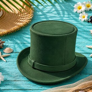 May include: A dark green top hat with a matching band sits on a turquoise wooden surface, surrounded by seashells, starfish, and flowers. A straw hat and sunglasses are also visible, suggesting a beach or vacation theme.