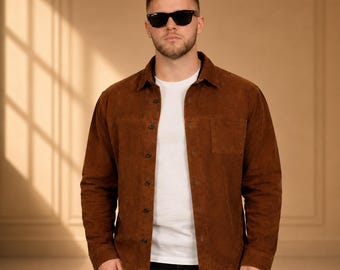 May include: A brown suede shirt with a button-down front and two chest pockets. The shirt is worn over a white t-shirt and paired with black pants. The person is wearing black sunglasses.