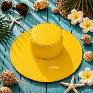 Puede incluir: Un sombrero de sol amarillo brillante con un ala de 15 cm. La imagen incluye gafas de sol, conchas marinas y flores tropicales, evocando un ambiente de playa o vacaciones. El dise&ntilde;o del sombrero es sencillo.