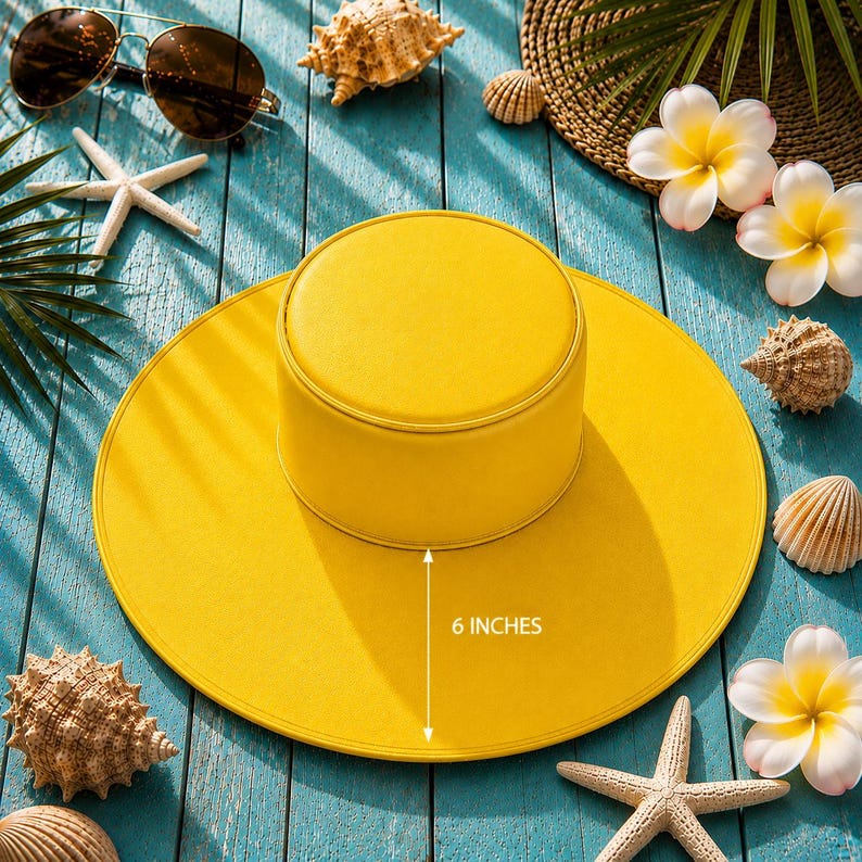 Puede incluir: Un sombrero de sol amarillo brillante con un ala de 15 cm. La imagen incluye gafas de sol, conchas marinas y flores tropicales, evocando un ambiente de playa o vacaciones. El dise&ntilde;o del sombrero es sencillo.
