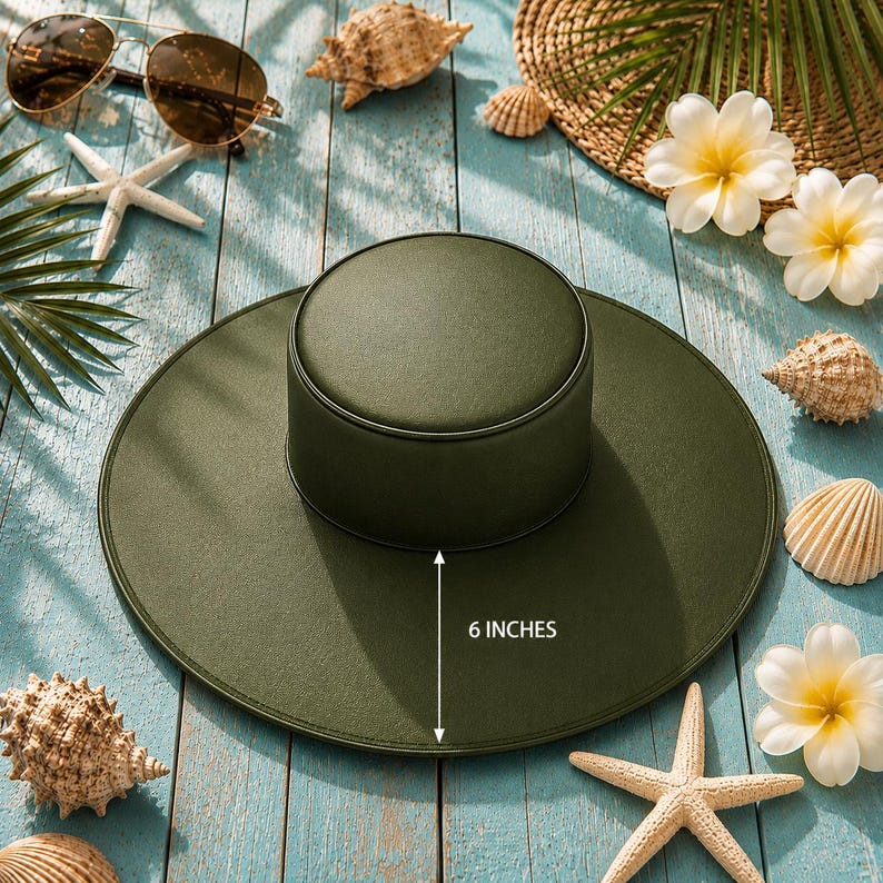 Puede incluir: Sombrero de sol verde oliva con una corona de 15 cm, rodeado de conchas, estrellas de mar y gafas de sol. El sombrero est&aacute; sobre una superficie de madera azul claro, evocando la playa.