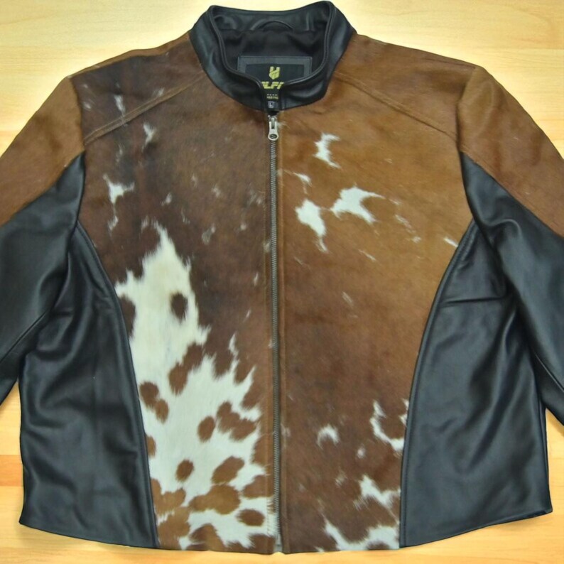 May include: A full-zip leather jacket with a cowhide front panel. The jacket features a brown and white cowhide pattern, black leather side panels, and a black leather collar. The jacket has a silver zipper and a small logo on the collar.
