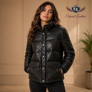 Könnte beinhalten: Schwarze Leder-Steppjacke mit hohem Kragen und silbernen Knopfverschlüssen. Die Jacke hat zwei Vordertaschen. Das Markenlogo "Eshaal Leather" ist in der oberen rechten Ecke sichtbar. Die Jacke wird von einer Person getragen.