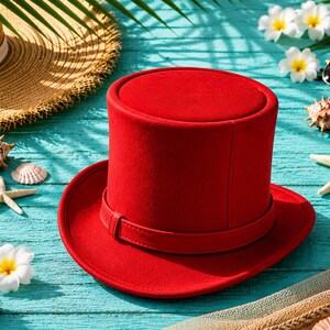 May include: A vibrant red top hat with a matching band, set against a turquoise background with seashells, starfish, and sunglasses. A straw hat is partially visible in the background, suggesting a beach theme.