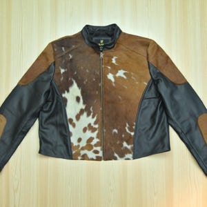 May include: A brown and black leather jacket with a cowhide pattern on the front. The jacket has a zipper closure and black leather sleeves and accents. The collar is black.