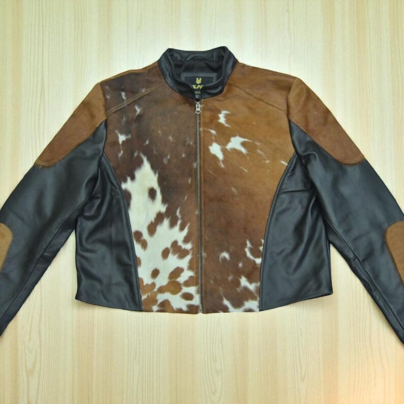 May include: A brown and black leather jacket with a cowhide pattern on the front. The jacket has a zipper closure and black leather sleeves and accents. The collar is black.