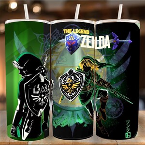 May include: A set of three stainless steel tumblers with white straws. Each tumbler features a different design from The Legend of Zelda video game. The designs include characters, shields, and the game's logo, set against green and black backgrounds.