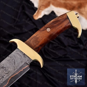 May include: Close-up of a large knife with a patterned blade and a wooden handle. The handle is a rich brown color with a gold-colored bolster and a small decorative emblem. The blade has a unique pattern.