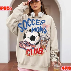 Puede incluir: Sudadera beige con un gráfico que dice "Soccer Moms Club". El gráfico incluye un balón de fútbol, botas de fútbol, una bebida y un lazo rosa. La sudadera es de manga larga.