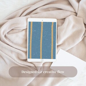 Puede incluir: Una tableta blanca muestra un fondo azul con dos rayas verticales doradas. La tableta descansa sobre una manta beige, con una tarjeta blanca. El texto "Designed for creative flow" es visible.