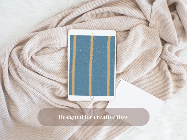 Puede incluir: Una tableta blanca muestra un fondo azul con dos rayas verticales doradas. La tableta descansa sobre una manta beige, con una tarjeta blanca. El texto "Designed for creative flow" es visible.