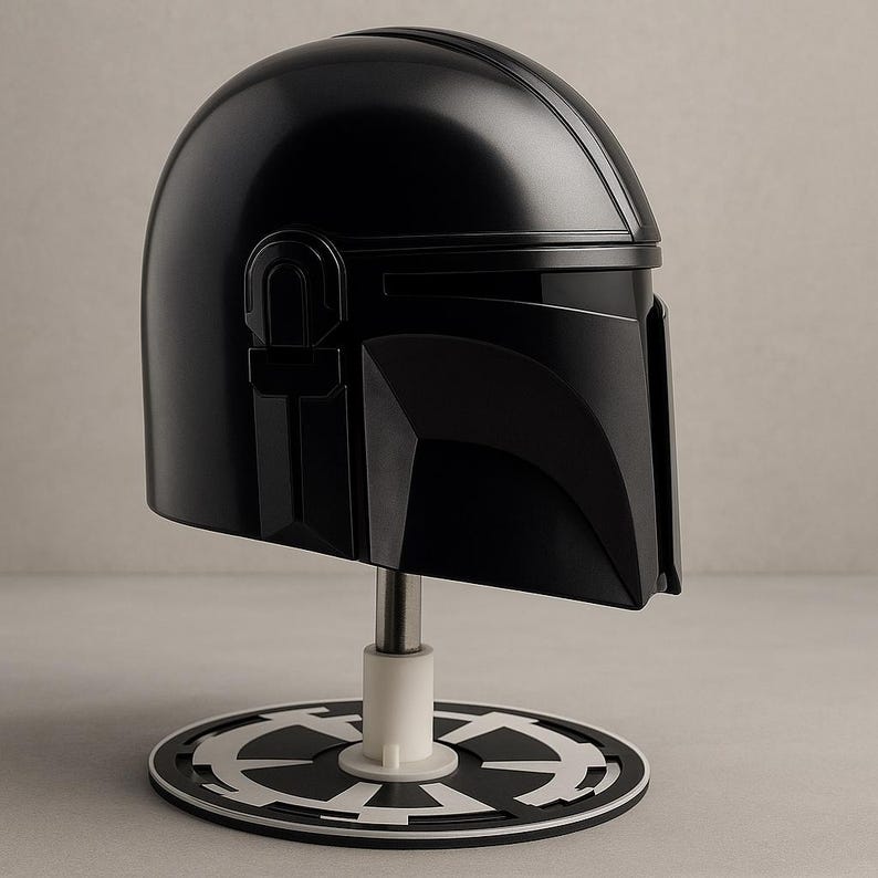 May include: A black Mandalorian helmet with a glossy finish, presented on a stand. The helmet has a T-shaped visor and unique detailing. The stand features a white base and a black and white emblem. A replica from the Star Wars series.