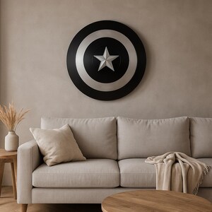 May include: A large, round shield with a black, silver, and white design, featuring a central star emblem. The shield is mounted on a neutral-toned wall above a beige sofa, creating a decorative accent.