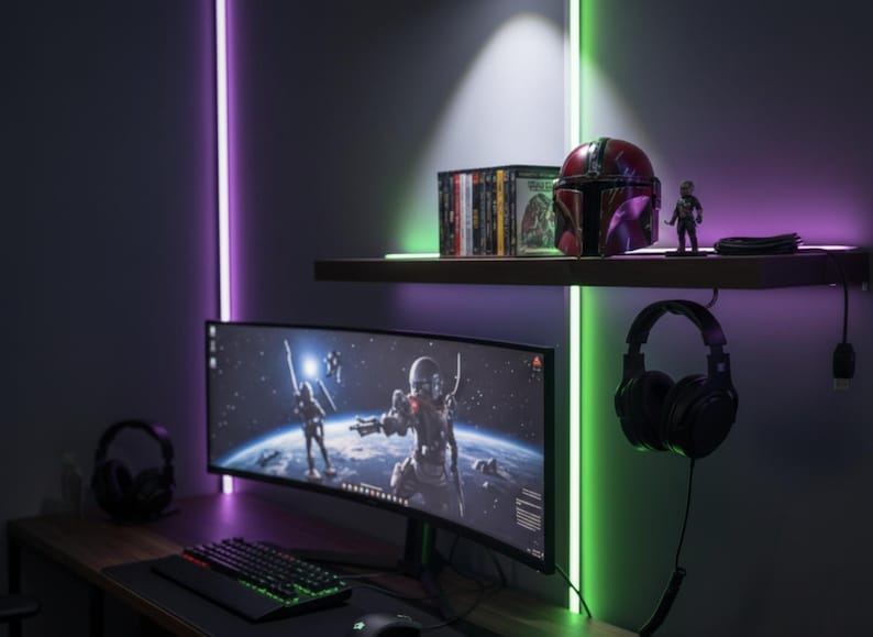 May include: A gaming setup featuring a curved monitor displaying a space battle scene. A keyboard, mouse, and headset are on the desk. A shelf above holds a Mandalorian helmet, action figure, and game discs. The wall has purple and green LED lights.