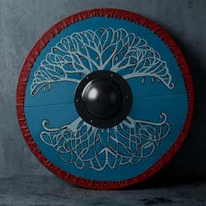 May include: A circular shield with a blue central panel, decorated with a white tree motif. The shield has a red rim with metal studs and a black central boss. Likely for display or costume purposes.