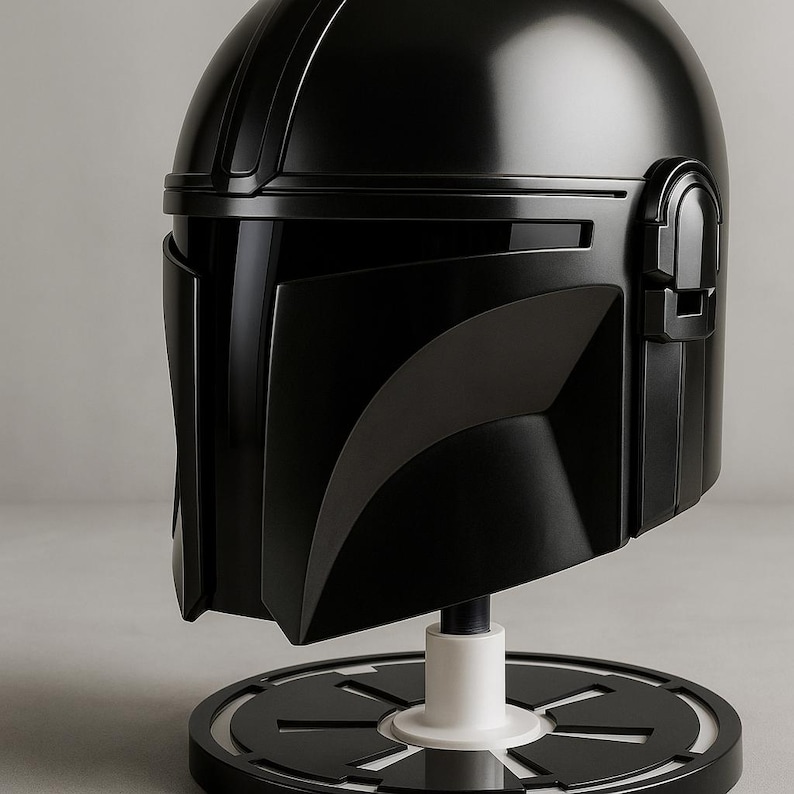 May include: A black Mandalorian helmet replica, presented on a black and white stand. The helmet has a glossy finish and detailed design, showcasing the iconic shape and visor.
