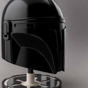 May include: A shiny black Mandalorian helmet, presented on a stand with a white and black emblem. The helmet has a sleek, angular design with a visor and distinctive curved lines. The stand has a white cylindrical base.