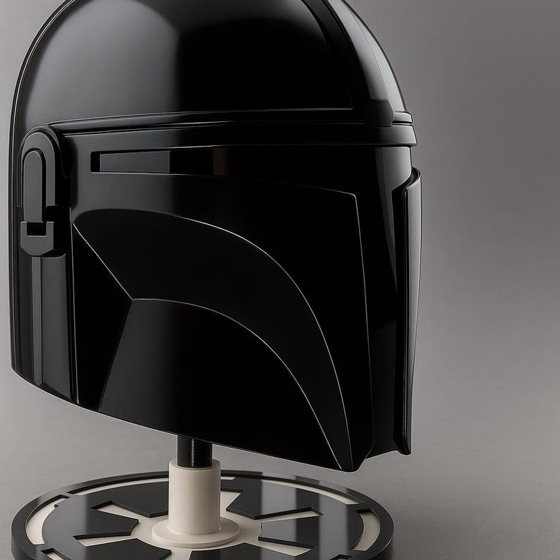 May include: A shiny black Mandalorian helmet, presented on a stand with a white and black emblem. The helmet has a sleek, angular design with a visor and distinctive curved lines. The stand has a white cylindrical base.