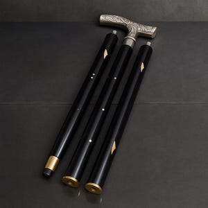 Puede incluir: Bastón plegable negro con un mango plateado con un diseño floral ornamentado. El eje del bastón está segmentado, con detalles dorados y elementos decorativos incrustados. El bastón está diseñado para brindar apoyo y estilo.