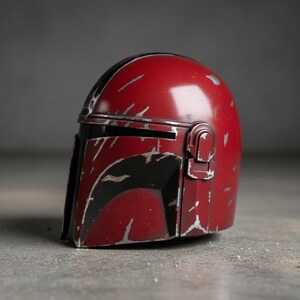 May include: A red Mandalorian helmet with black accents and silver weathering details. The helmet features a visor and a distinctive T-shaped opening. This collectible item is a replica of the iconic helmet from the Star Wars series.