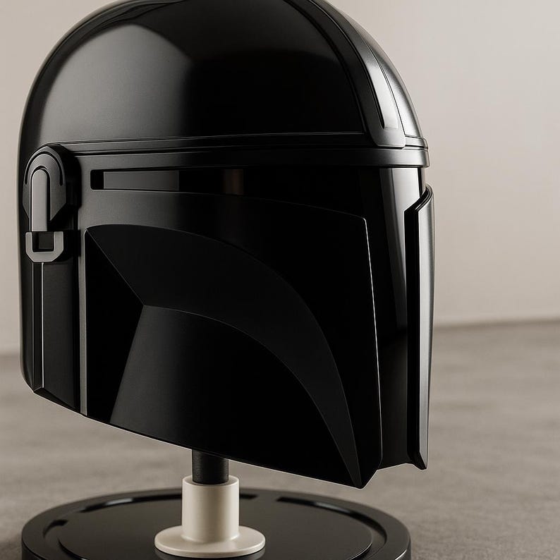 May include: A shiny black Mandalorian helmet, presented on a black and white stand. The helmet has a distinctive T-shaped visor and angular design, exhibiting a sleek, futuristic aesthetic. The helmet is a collectible item.