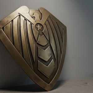 Pode incluir: Um escudo de cor bronze com um emblema de &aacute;guia e uma estrela. O escudo tem um design detalhado com padr&otilde;es de asas e formas geom&eacute;tricas. O escudo est&aacute; inclinado, mostrando seu artesanato intrincado e acabamento met&aacute;lico.