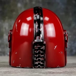 May include: A red helmet with a black stripe down the center and black accents. The helmet has a distressed finish with visible wear and tear. The design is reminiscent of a space-themed helmet.