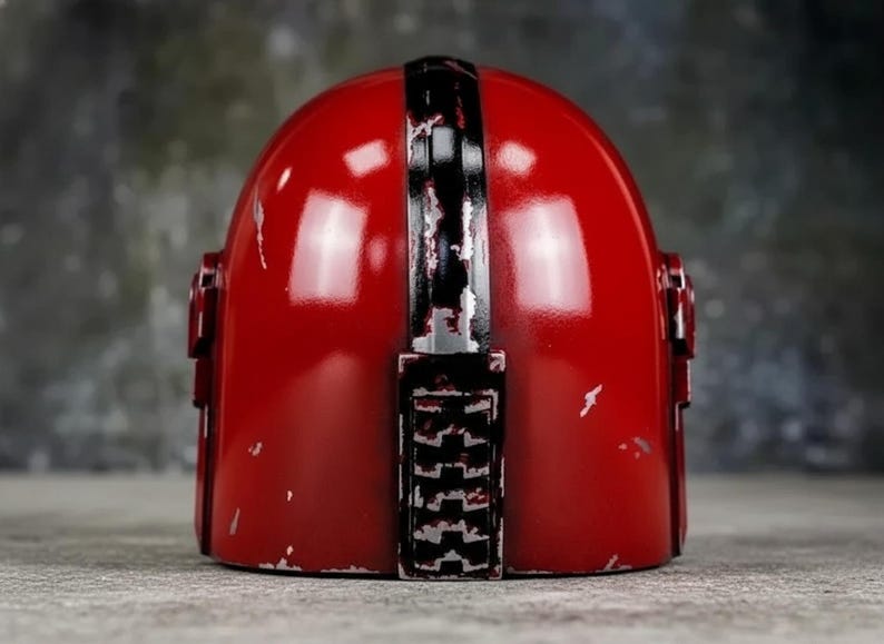 May include: A red helmet with a black stripe down the center and black accents. The helmet has a distressed finish with visible wear and tear. The design is reminiscent of a space-themed helmet.