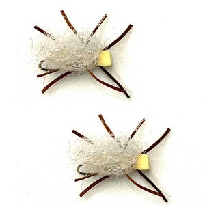 May include: Two handmade fishing flies. Each fly features a central fluffy, off-white body, a small yellow square, and several brown, radiating appendages. The flies are set against a plain white background, showcasing their intricate design.