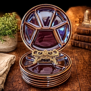 May include: A stack of dark purple ceramic plates with a glossy finish and a segmented design featuring five distinct compartments. The plates are held upright by an ornate, metallic gold-colored display stand with intricate scrollwork details.