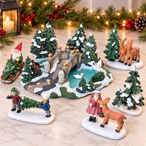May include: A miniature Christmas village set featuring a stone bridge over a blue pond, snow-dusted pine trees, a gnome on a sled, two children carrying a tree, a person with a deer, and two standing deer figures, all on white snowy bases.