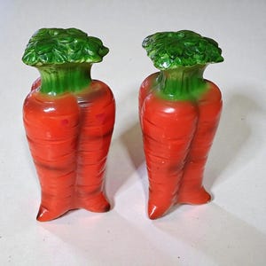 May include: Two carrot-shaped salt and pepper shakers. The shakers are orange with green leafy tops. The carrot shakers are ceramic and have a glossy finish. The shakers are designed to look like a pair of carrots.