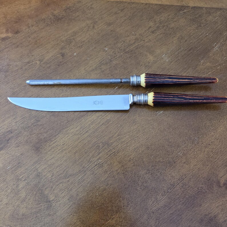 May include: A stainless steel carving knife and sharpening steel set. The knife has a curved blade and a handle with a dark brown and cream-colored design. The sharpening steel has a similar handle design.