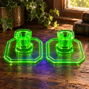 Op de afbeelding: Een paar fel neon-groene glazen kandelaars met een achthoekige voet en een bijpassende achthoekige houder. Het doorschijnende materiaal gloeit intens en toont een geometrisch ontwerp met strakke, scherpe randen en een glad, gepolijst oppervlak.