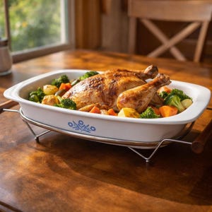 May include: A roasted chicken with vegetables in a white casserole dish with blue floral accents. The dish sits on a metal rack with wooden handles, placed on a wooden table. Broccoli, carrots, and potatoes surround the chicken.