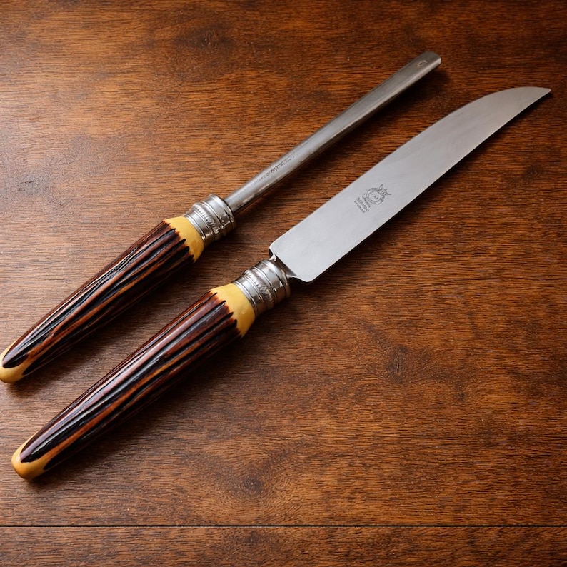 May include: A knife and sharpening steel set. The knife has a curved blade and a handle with brown and cream tones. The sharpening steel has a similar handle design. Both pieces have silver-colored metal accents.
