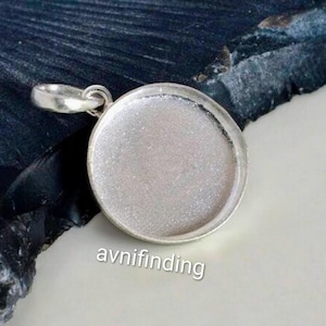 May include: A silver-coloured round pendant base with a loop for a chain. The pendant has a recessed area for adding a design or image. The text "avnifinding" is printed on the bottom right.