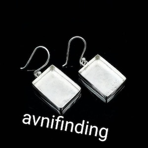 Può includere: Un paio di monachelle per orecchini in metallo color argento con castoni rettangolari a centro aperto e ganci curvi. Gli orecchini hanno una finitura metallica liscia e sono mostrati su uno sfondo nero con il testo avnifinding.