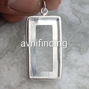 Peut inclure: Un pendentif rectangulaire en argent avec une ouverture rectangulaire au centre. Le pendentif a une petite boucle en haut pour une chaîne. Le texte "avnifinding" est imprimé en blanc sur le pendentif.
