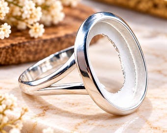 Può includere: Una montatura per anello in tonalità argento lucido con un castone ovale liscio progettato per un cabochon o una pietra preziosa. La fascia presenta un design a gambo diviso che si collega ai lati della cornice ovale centrale.