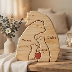 Op de afbeelding: Een lichtgekleurde houten puzzel met vier in elkaar grijpende beervormen. De beren zijn gegraveerd met de namen Mommy, Daddy, Luna en Jack. Een klein rood hartje is geplaatst tussen de twee kleinere beren. De houtnerf is duidelijk zichtbaar.