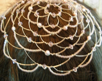 May include: A delicate, silver-toned headpiece with a web-like design. The headpiece is adorned with small, clear beads and larger, pearlescent beads. The intricate wirework creates a graceful, circular pattern, suitable for special occasions.
