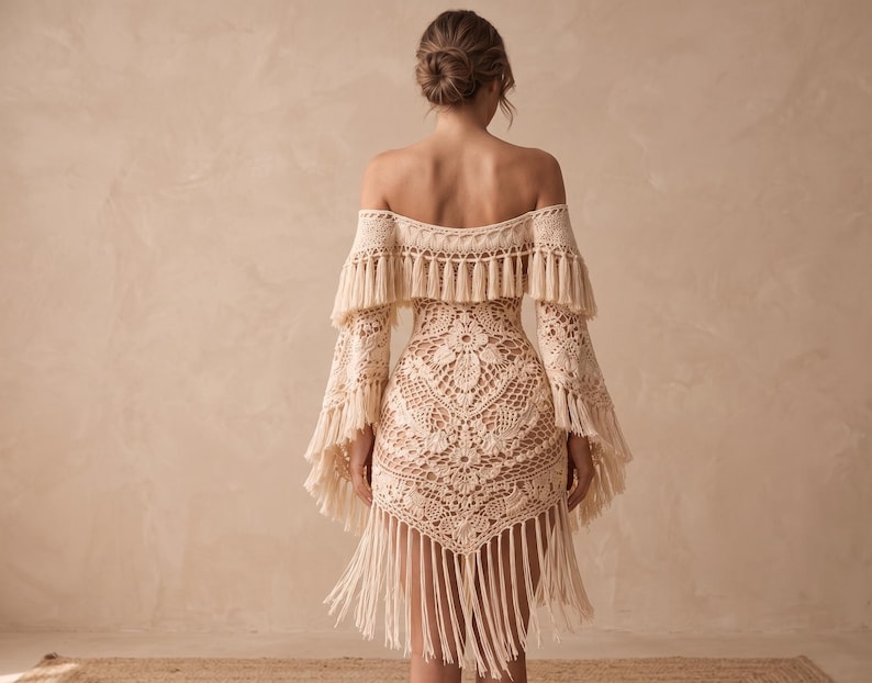 May include: A cream-colored, off-the-shoulder crochet dress with long sleeves and fringe detailing. The dress features a floral pattern on the bodice and a fringed hemline. The sleeves have a bell shape and are adorned with fringe.